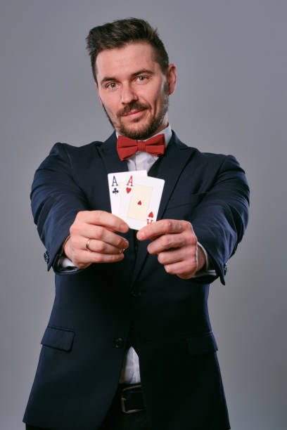 istock Man in black classic suit and red bow-tie showing two playing cards while posing against gray studio background. Gambling, poker, casino. Close-up 1210115980