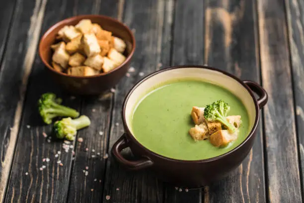 Broccoli cream soup with croutons in a plate on a wooden black background.  Concept of healthy nutrition. Close up. Horizontal orientation.