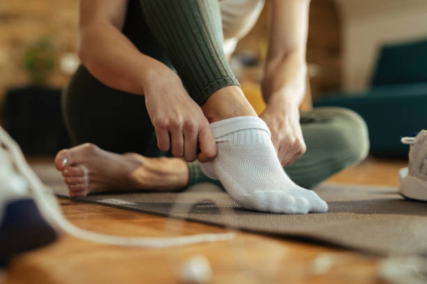 Close-up of athletic woman putting on socks. Close-up of sportswoman wearing white socks while preparing for workout at home. getting dressed stock pictures, royalty-free photos & images