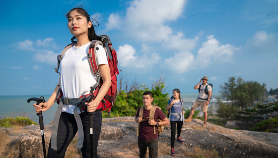 Group of hikers walking in mountains. Young happy travelers hiking with backpacks on the beautiful rocky trail at warm sunny evening. Trek hiking destination experience lifestyle concept