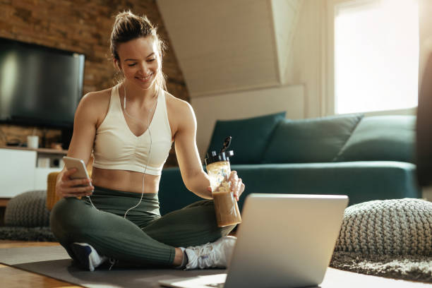 istock Happy sportswoman drinking protein shake while using laptop at home. 1210122066