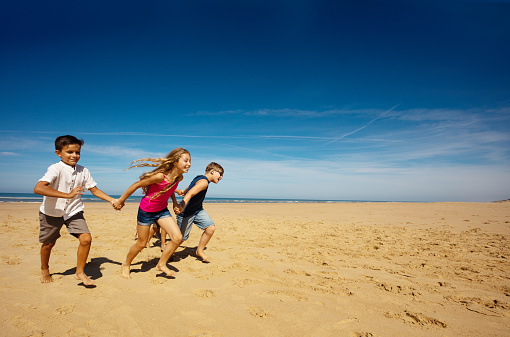 Group of kids boys and girls run fast for fun on the beach together holding hands