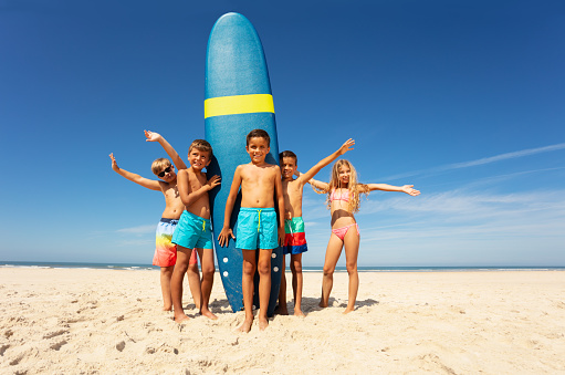 Group happy little kids stand by surfboard to the sea together on the beach and wave hands