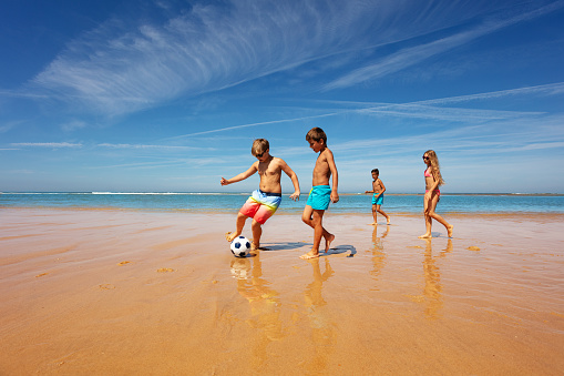 Kids in the middle of soccer game play on a sea beach near the water