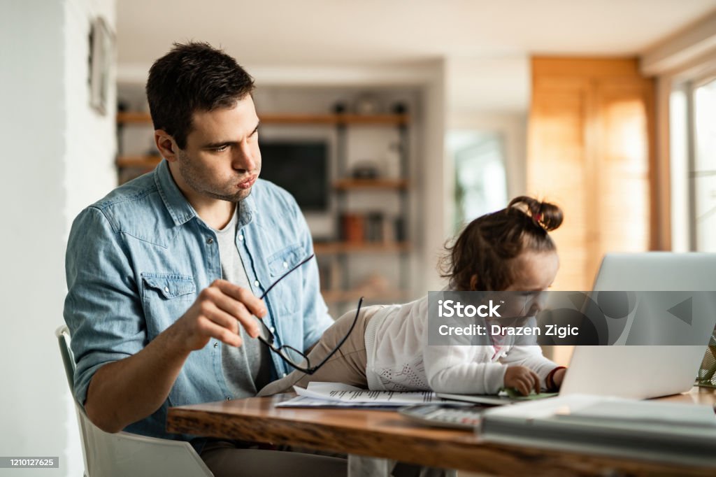 Babysitting and working at home! Stay at home father feeling stressed while baby sitting and trying to work while his small daughter is using his laptop. Working At Home Stock Photo