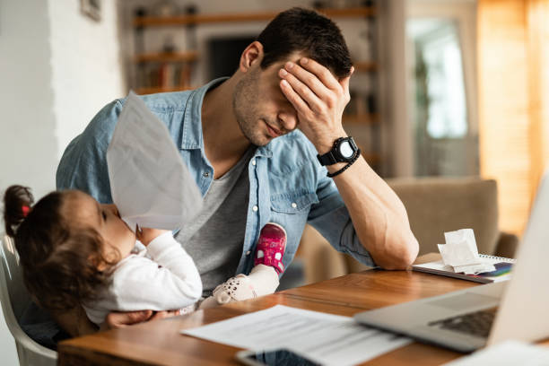 Stay at home father having a headache while babysitting and working at home. Young father feeling exhausted and having a headache while babysitting his small daughter and working at home. Tensed stock pictures, royalty-free photos & images