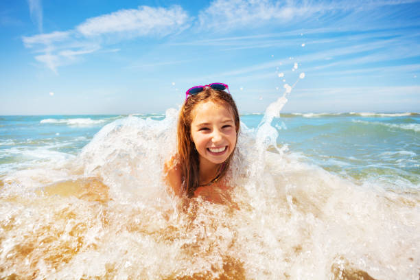 istock Cute girl being hit by a wave playing on sea beach 1210129078