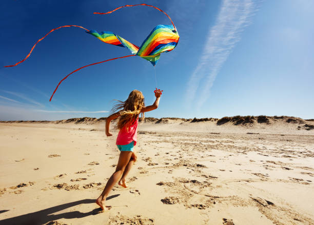 istock Girl run fast on beach hold color kite back view 1210129179