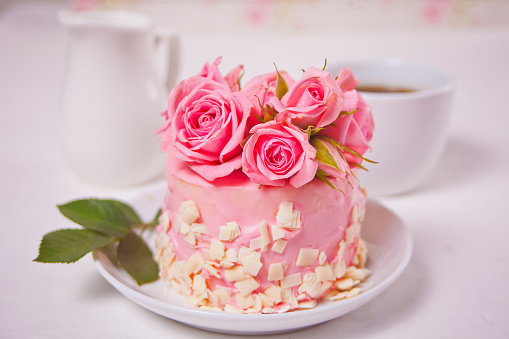 Mini cake with pink glaze, beautiful roses, cup of coffee, gift box on the white table