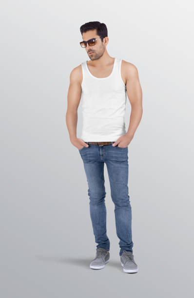 Standing male model wearing plain white tank top shirt in blue denim jeans pant Fitness man wearing blank sleeveless shirt and sunglasses on isolated background sleeveless top stock pictures, royalty-free photos & images