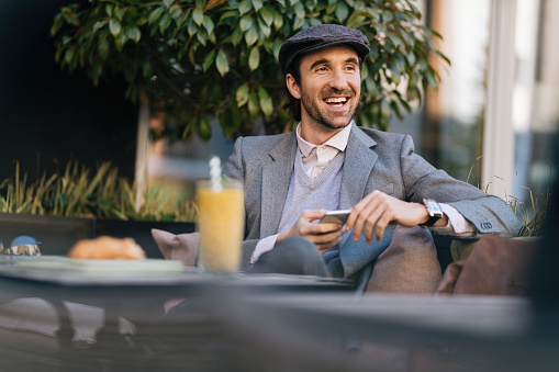 Young happy entrepreneur texting on smart phone while sitting in outdoor cafe.