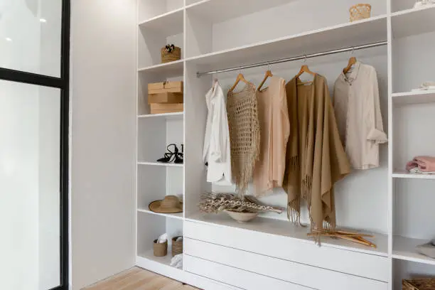 Side view on open space minimalistic scandinavian white wood walk in closet and wardrobe in neutral beige colors