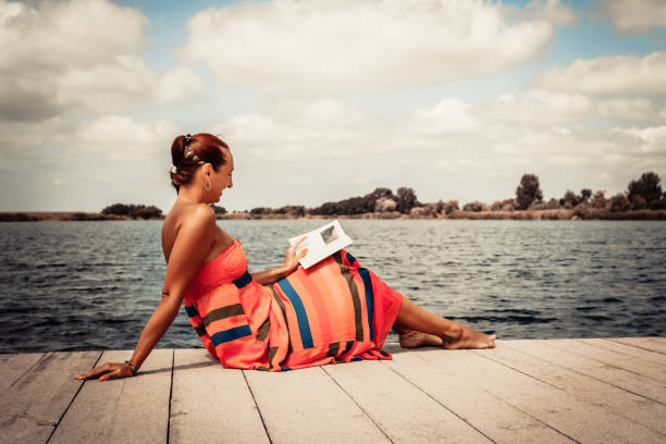 Happy woman relaxing on a pier and reading book during summer day at the beach.