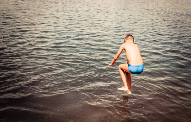 istock Playful boy jumping in the water during summer day. 1210136086
