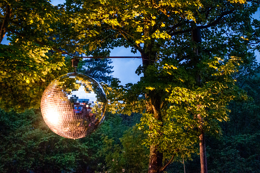 Light shining onto a large mirror ball, suspended outdoors in a forest setting.