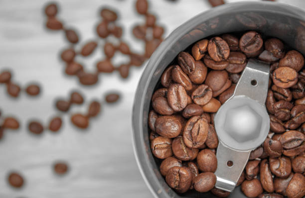 Top view of an electric coffee grinder with coffee grains poured into it. Blurred background with grains of coffee Top view of an electric coffee grinder with coffee grains poured into it. Blurred background with grains of coffee. blade roast stock pictures, royalty-free photos & images