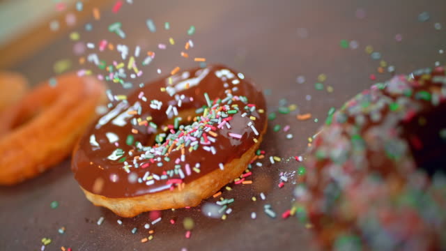 SLO MO LD Sprinkles falling onto a chocolate covered donut