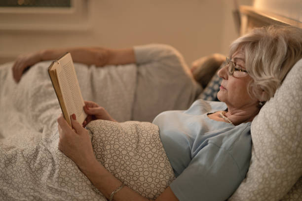 istock Senior woman reading a book while resting in bed in the evening. 1210140552