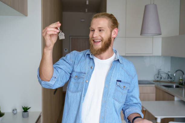 Happy young man renter first time home owner holding key to new apartment Happy young single man tenant renter first time home owner holding key to new apartment, excited male house buyer customer moving into own flat, buying real estate mortgage investment purchase concept independence document agreement contract stock pictures, royalty-free photos & images