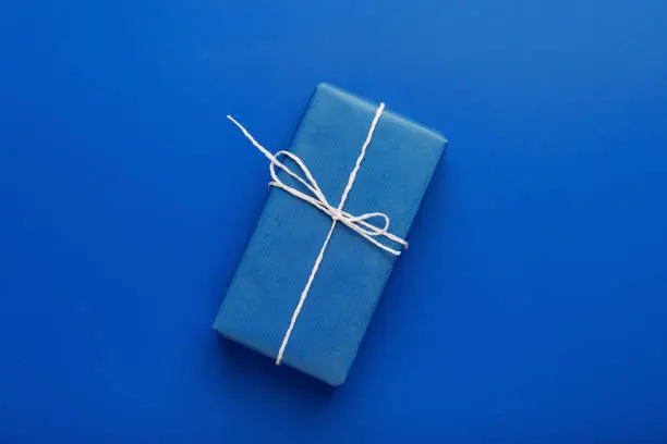 Gift blue box with white bow on a blue background. Top view. Minimal style