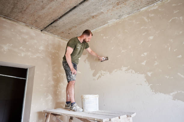 le constructeur se tient sur le support en bois et travaille avec la spatule avec le plâtre au mur dans la petite pièce - plasterer plaster wall dirty photos et images de collection