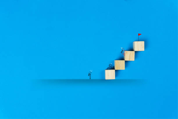 istock Each person's differences about success concept. A simple line art businessman going to the red flag on top of wooden block on blue background. 1210161412
