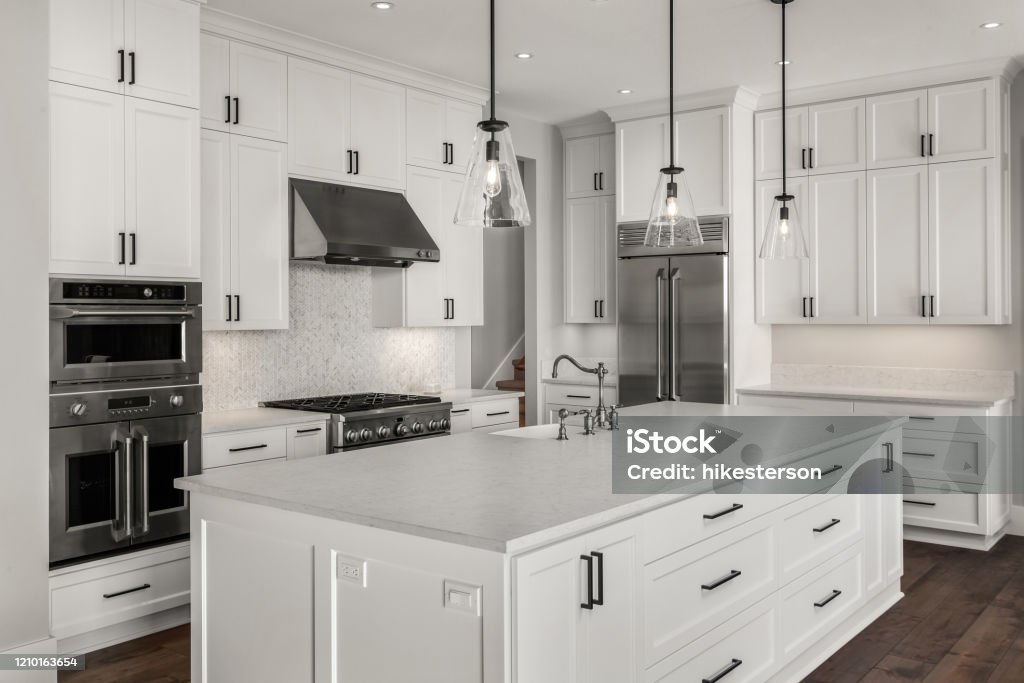 Beautiful kitchen in new luxury home with island, pendant lights, and hardwood floors. Features stainless steel appliances, including double oven, refrigerator, gas range and hood. kitchen in newly constructed luxury home Kitchen Stock Photo