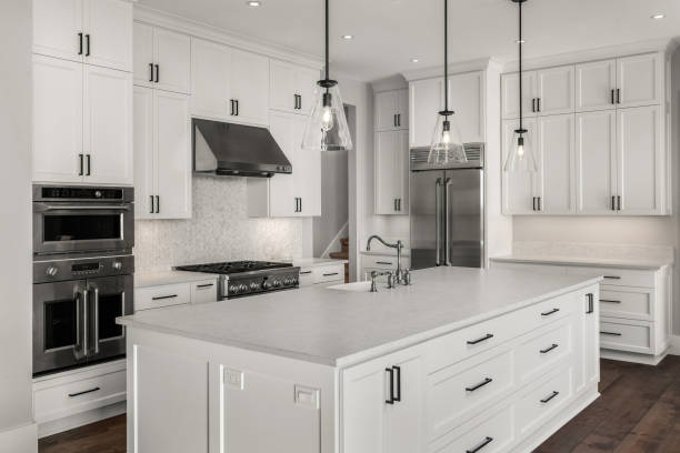 Beautiful kitchen in new luxury home with island, pendant lights, and hardwood floors. Features stainless steel appliances, including double oven, refrigerator, gas range and hood. stock photo