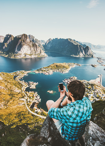 Man tourist taking selfie by smartphone on cliff Travel lifestyle concept adventure outdoor in Norway Reinebringen mountains aerial view Lofoten islands summer vacations