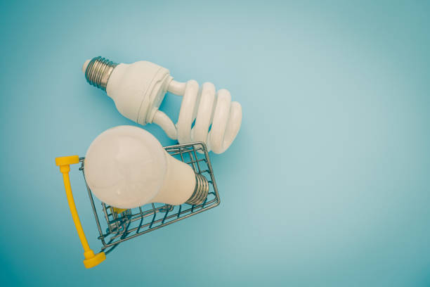 istock Fluorescent and LED light bulb with mini shopping cart or trolley on blue background for energy savings concept 1210168922