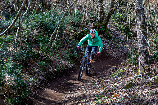 Rocca di Papa, Italy - February 29, 2020: Mountain bike cyclist runs on the country path, pedaling quickly downhill. Around him the thick vegetation with trees and green leaves on a spring day.