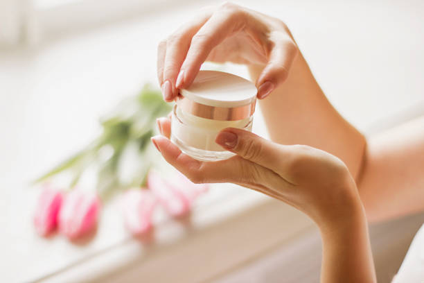 Woman's hands holding jar of face cream in hands Closeup of young woman's hand holding jar of moisturizing cream in hands with spring flowers tulips on background. Gentle girl opening jar with face lotion in arms. Beauty treatment, skin or body care face cream stock pictures, royalty-free photos & images