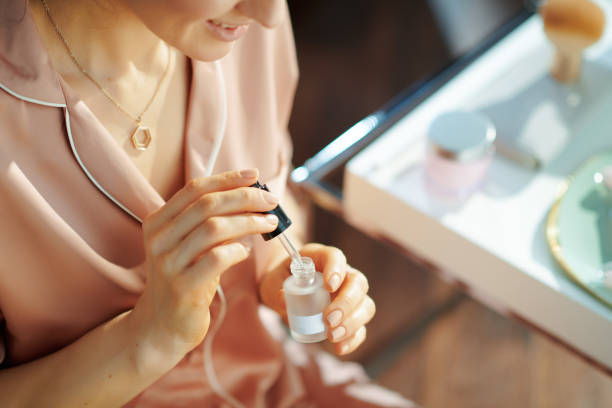 woman at modern home in sunny winter day using cosmetic elixir Closeup on smiling modern woman in pajamas at modern home in sunny winter day using cosmetic elixir. hair care women mature adult human skin stock pictures, royalty-free photos & images