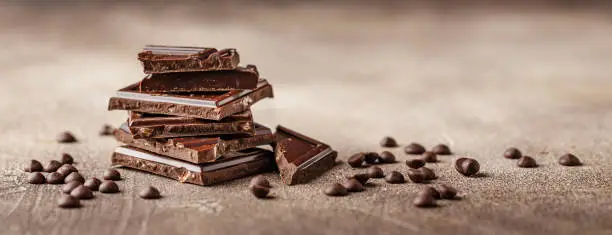 Slices of dark chocolate with chocolate chips on brown background close-up. Long wide banner