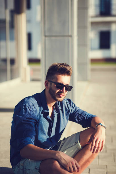 Handsome man in a shirt and sunglasses is sitting in the city