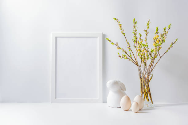 istock Home interior with easter decor. Mockup with a white frame and willow branches in a vase on a light background 1210178790