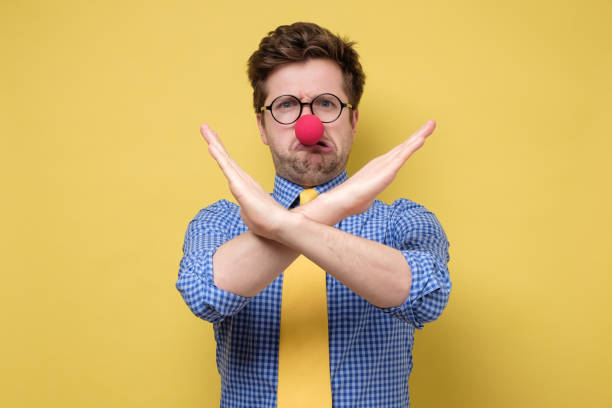 man with red clown nose over isolated yellow background making stop gesture Funny caucasian man with red clown nose over isolated yellow background making stop gesture. First April concept clown's nose stock pictures, royalty-free photos & images