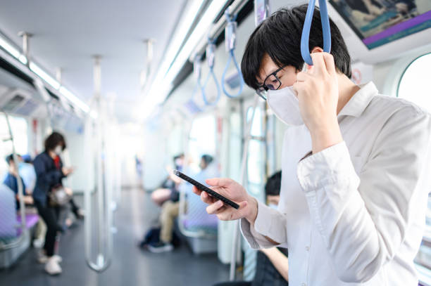 azjatycki mężczyzna w masce za pomocą telefonu na skytrain - bangkok mass transit system zdjęcia i obrazy z banku zdjęć