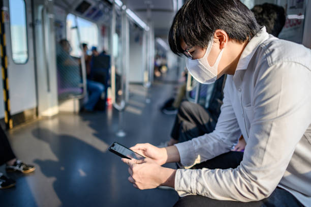 azjatycki mężczyzna w masce za pomocą telefonu na skytrain - bangkok mass transit system zdjęcia i obrazy z banku zdjęć