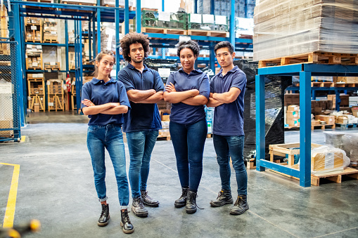 Group portrait of staff at distribution warehouse. Warehouse team standing with arms crossed in factory.