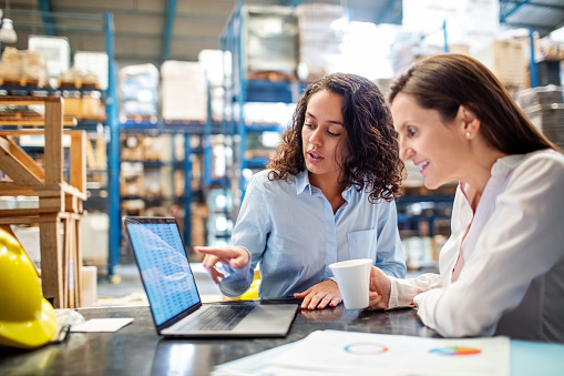 Woman showing inventory on laptop to warehouse manager
