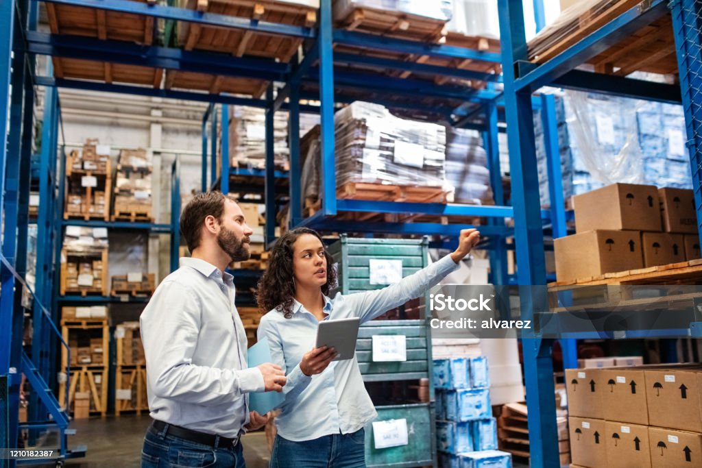 Manager and supervisor taking inventory in warehouse Businesswoman with a digital tablet showing and talking with male worker in distribution warehouse. Manager working with foreman in warehouse checking stock levels. Freight Transportation Stock Photo