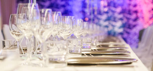 istock Table setting with a white tablecloth. A row of glass goblets and silver dishes 1210188433