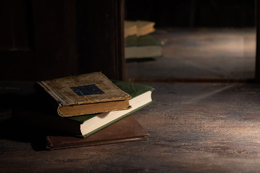 Three old books on a wooden table are reflected in an old mirror