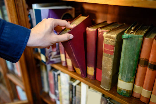 istock Male hand picking vintage book from bookshelf 1210196405