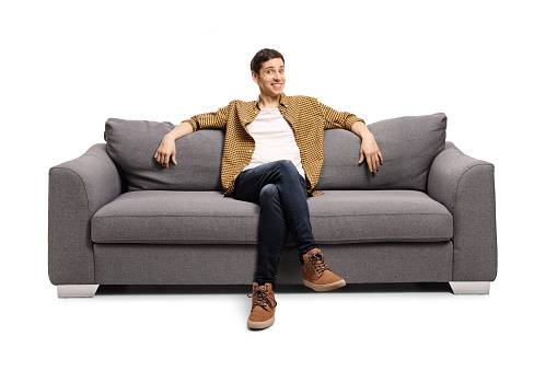 Young man sitting on a gray sofa isolated on white background