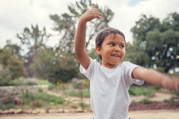 uma criança latina com os braços para cima em uma pose de dança flamenco espanhola, dançando ao ar livre em um jardim forrado de árvores. - child dancing preschooler outdoors - fotografias e filmes do acervo