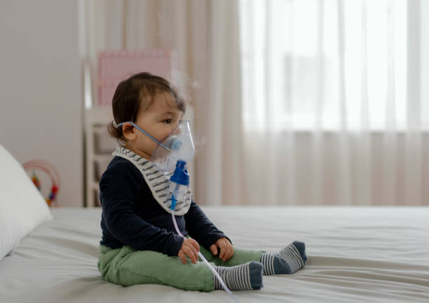 menino fofo com máscara de inalação sentado na cama - vapor da respiração - fotografias e filmes do acervo