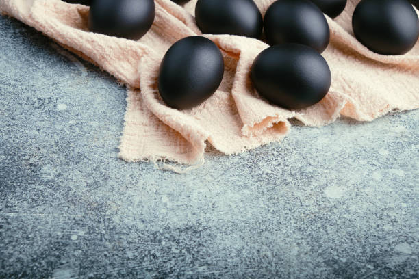 istock Black Easter eggs on a linen napkin on a blue texture table. Easter celebration concept. Copy space 1210202794