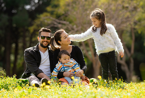 Happy family with male and female children cheering at park, Spring flowers and daisies can be seen all around the park